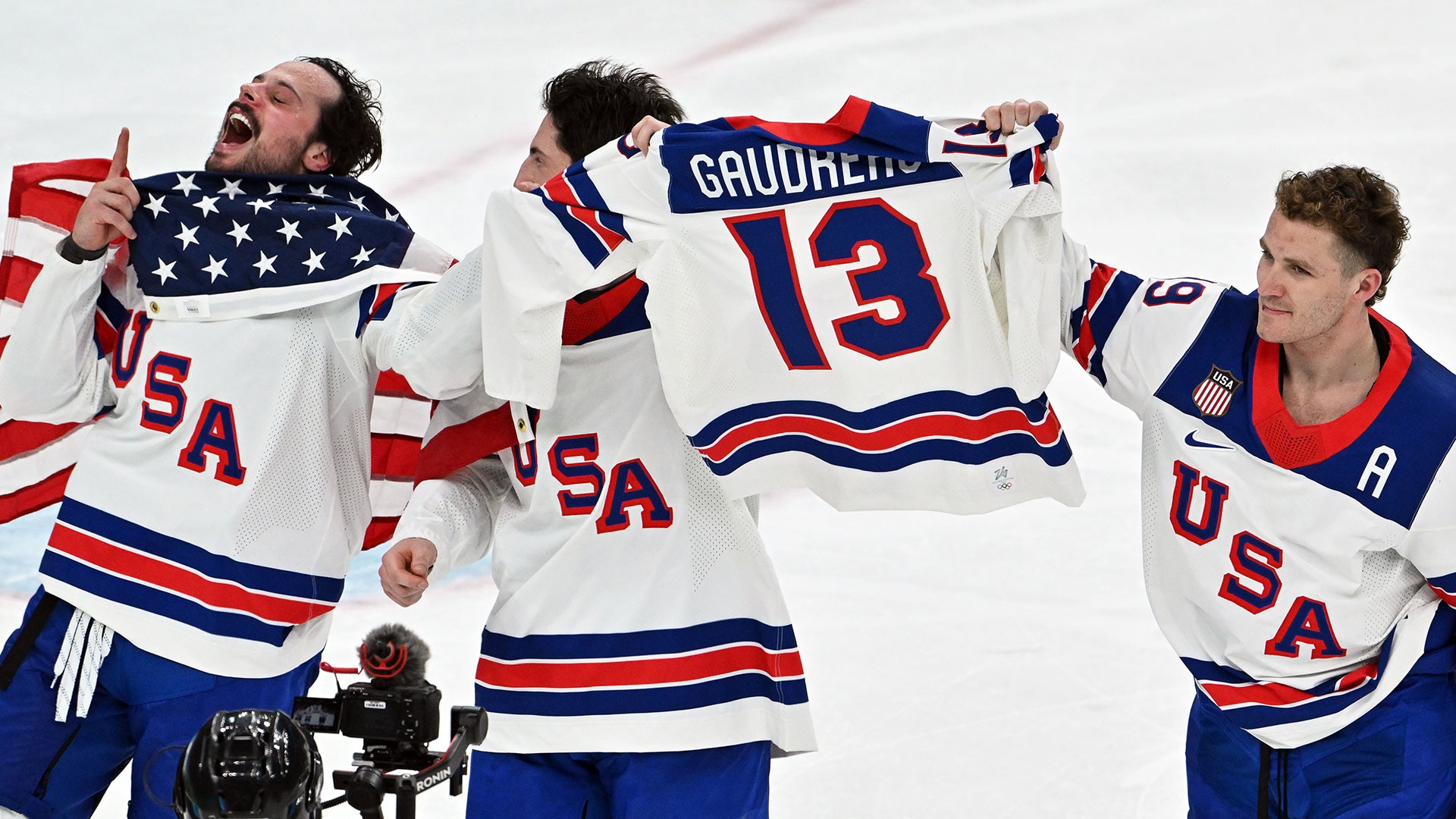 Auston Matthews, Zach Werenski and Matthew Tkachuk celebrate with their late teammate Johnny Gaudreau's jersey after winning gold over Canada at the 2026 Milan Cortina Olympics