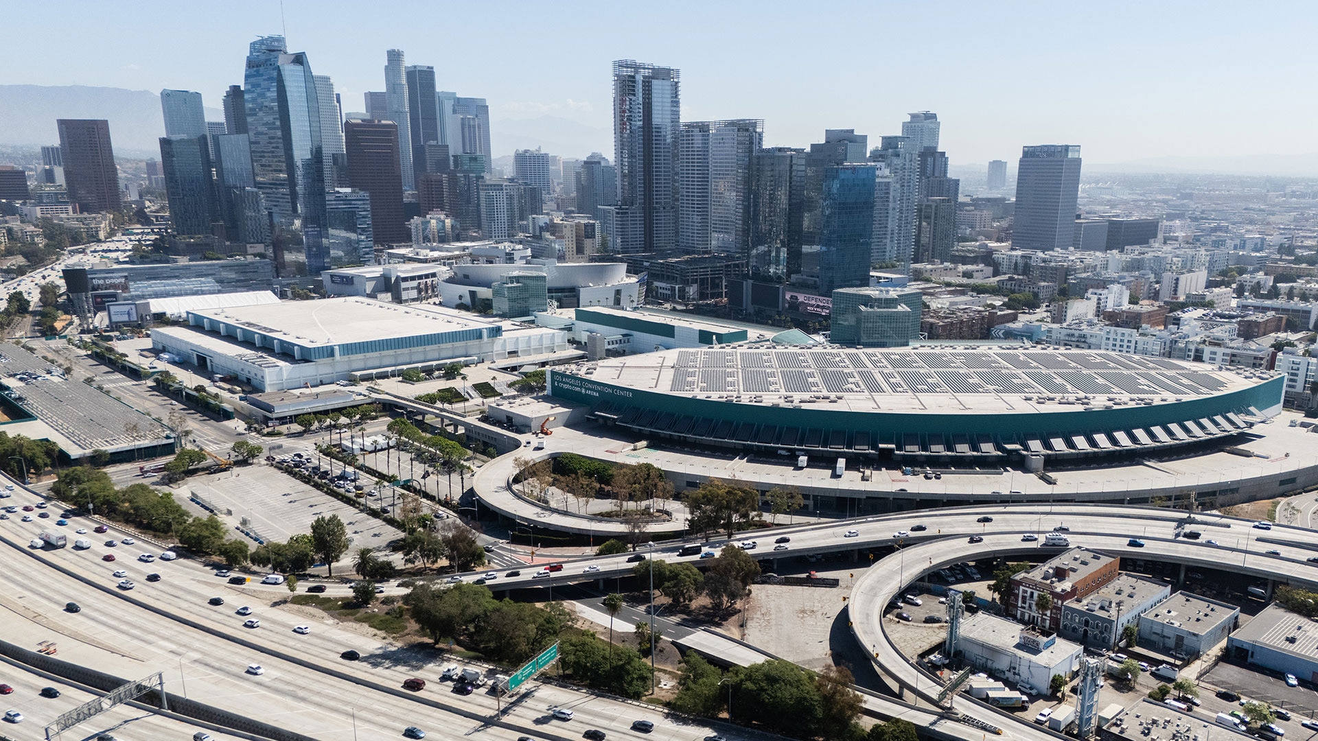An aerial shot of the Los Angeles Convention Center, sitting between a highway and the Los Angeles skyline
