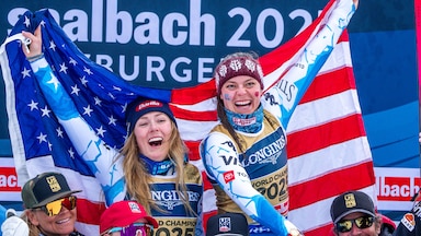Mikaela Shiffrin and Breezy Johnson celebrate after winning gold in the team combined event at the 2025 World Alpine Skiing Championships by holding the U.S. flag high.