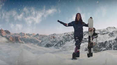 Brenna Huckaby poses on the top of a mountain with her snowboard.