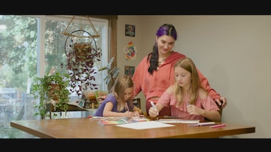 Brenna Huckaby stands with her daughters at the kitchen table.